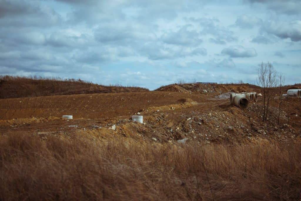 Serene rural landscape featuring earth mounds, overcast sky, and scattered pipes.